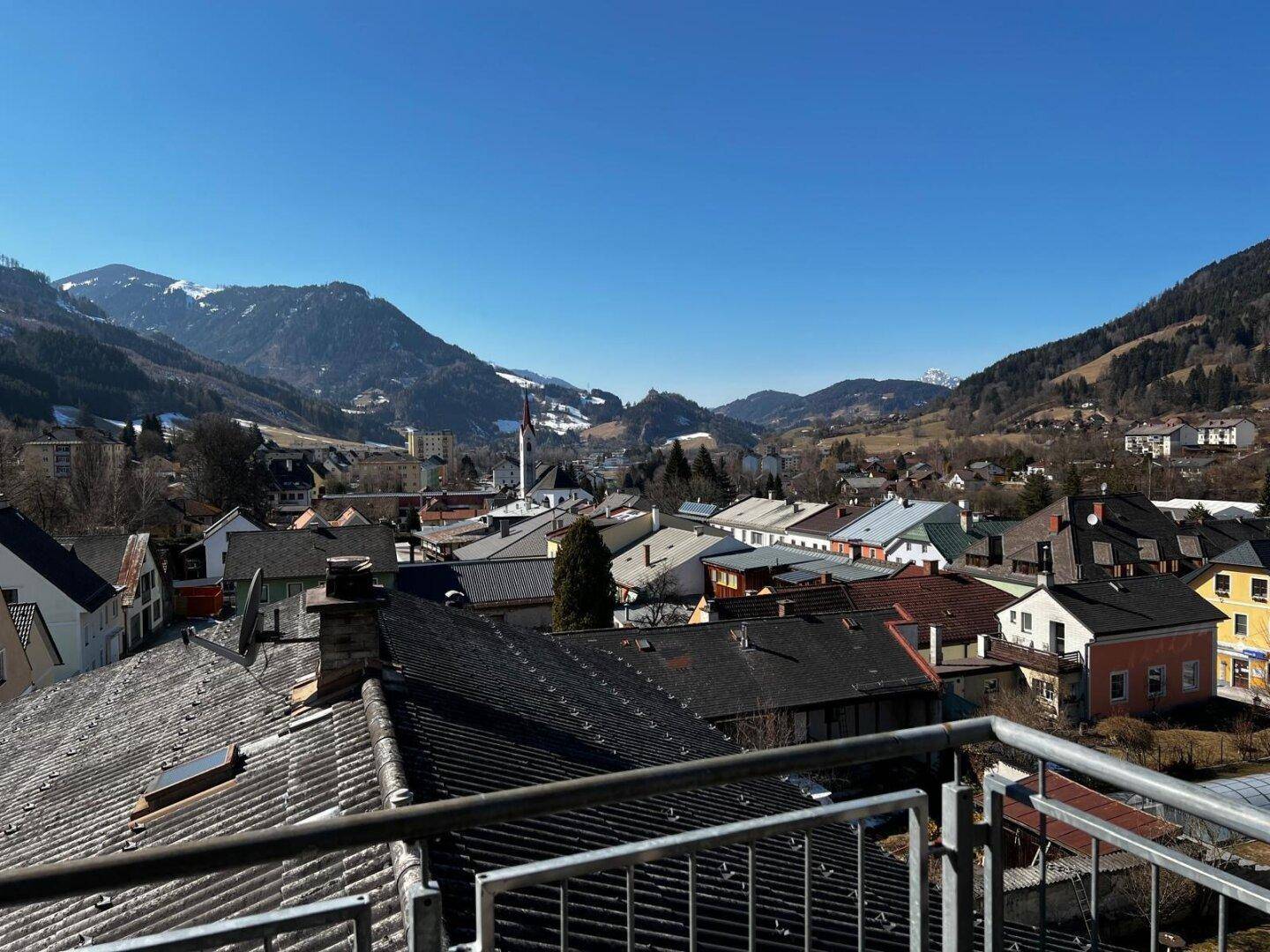 Panoramablick vom Balkon auf eine malerische Berglandschaft und die Dächer der Stadt.