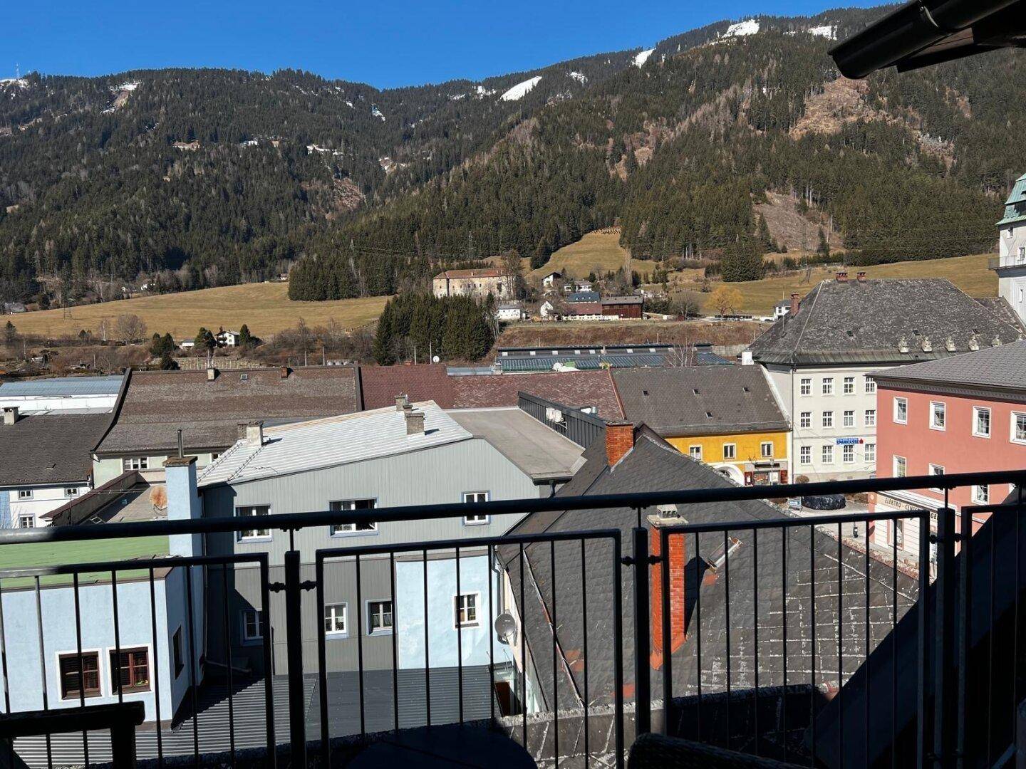 Weitläufiger Blick vom Balkon auf eine grüne Berglandschaft und die umliegenden Häuser.
