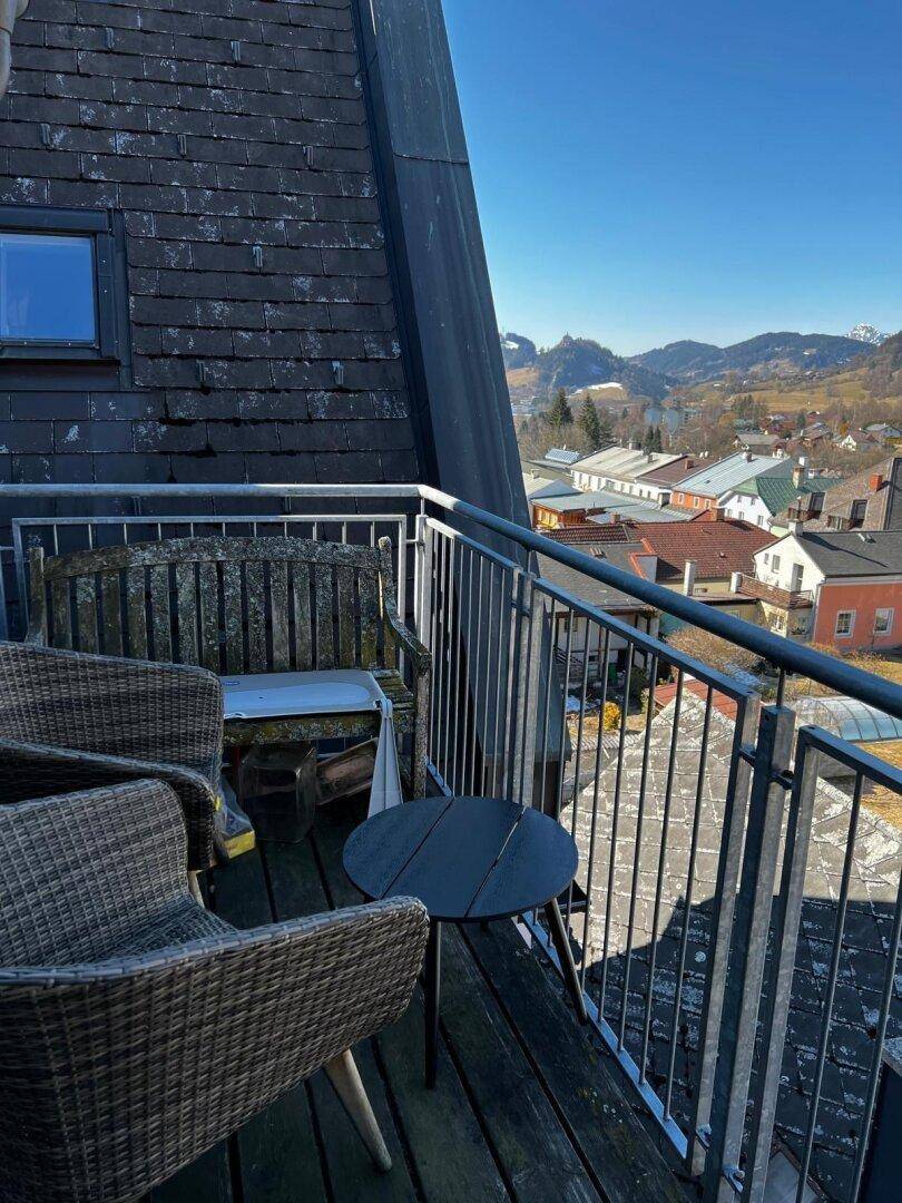 Gemütlicher Balkon mit Korbmöbeln und weitem Blick über die Dächer und Berge.