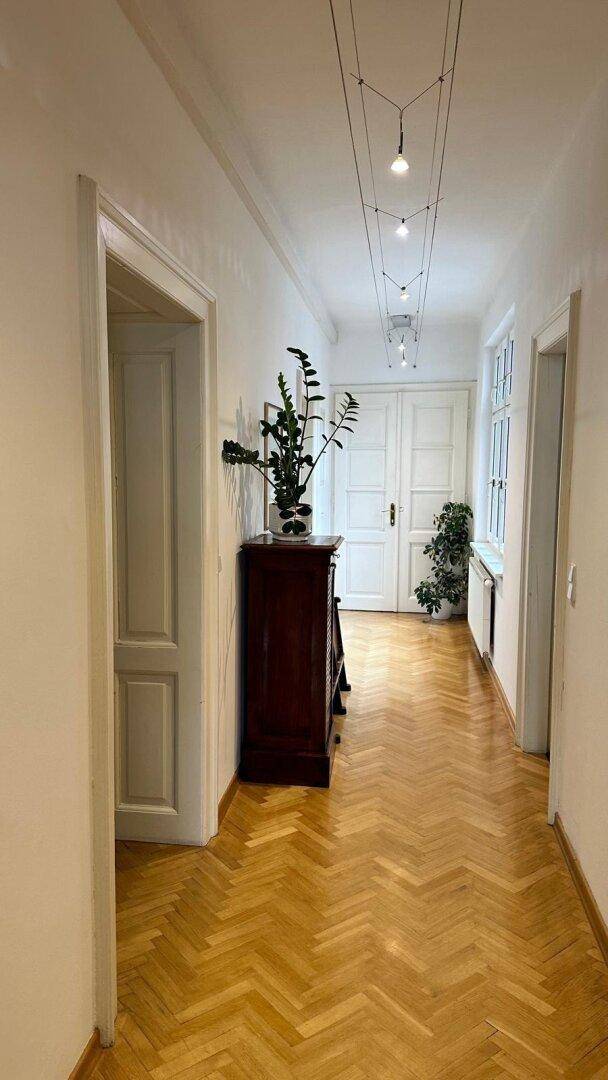Heller Flur mit Fischgrätparkett, einem antiken Schrank und Blick auf eine weitere Tür.