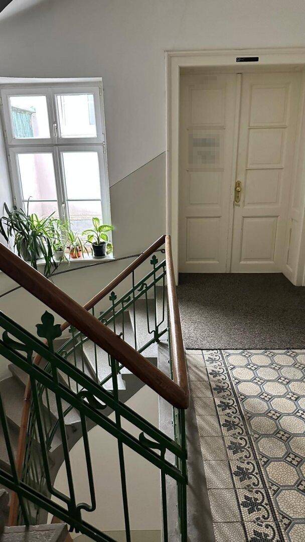 Treppenhaus mit traditionellen Fliesen, grünem Geländer und einem Fenster mit Pflanzen.