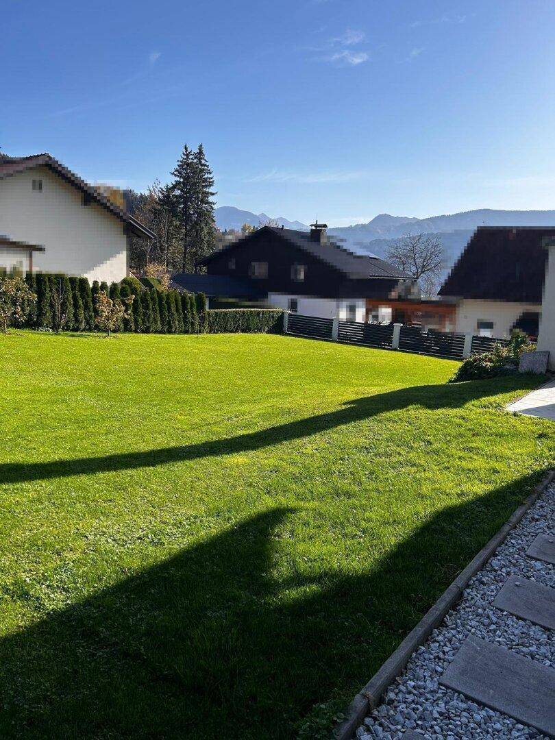 Gepflegter Rasen und Hecke vor einer Bergkulisse an einem klaren, sonnigen Tag.