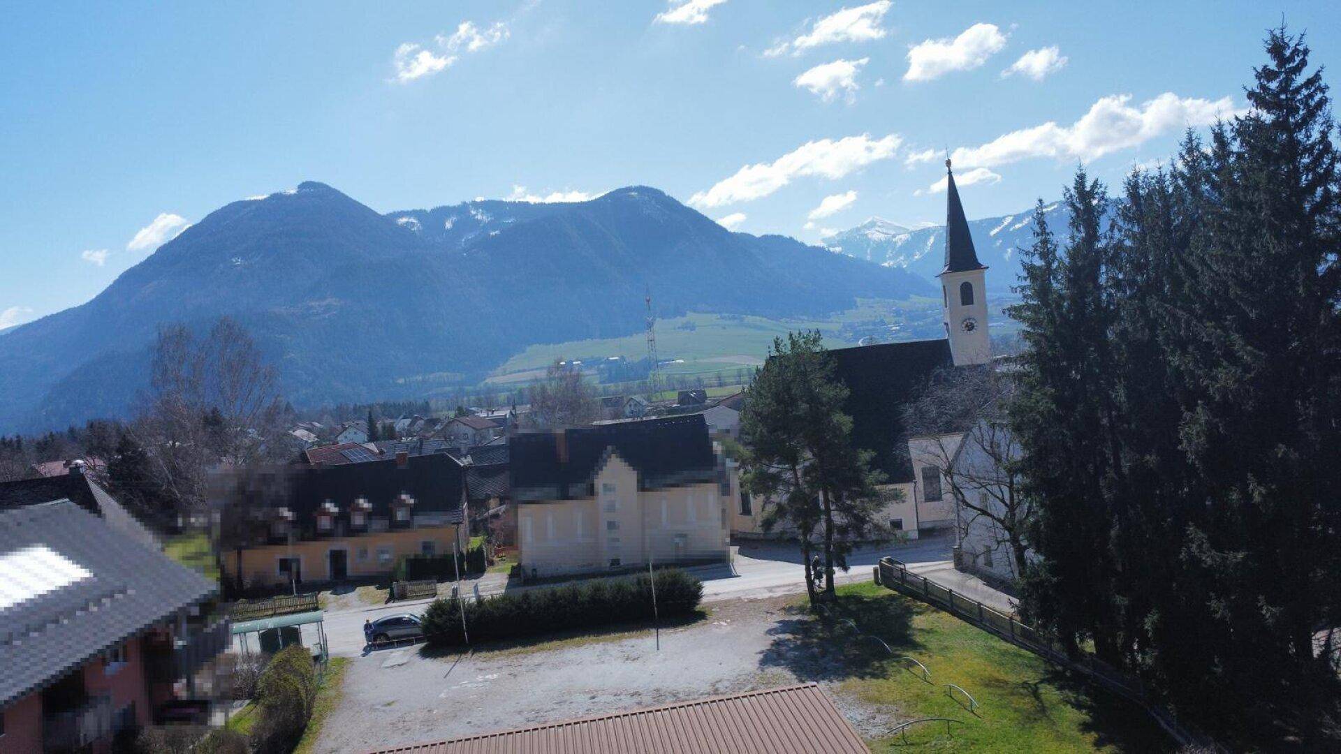 Panoramablick auf ein malerisches Dorf mit Kirche und schneebedeckten Bergen im Hintergrund.