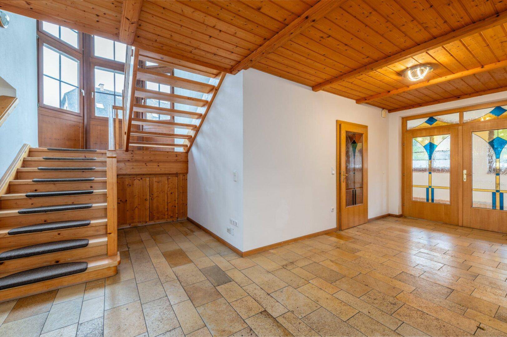 Geräumiger Eingangsbereich mit Holztreppe, Fliesenboden und dekorativen Glastüren.