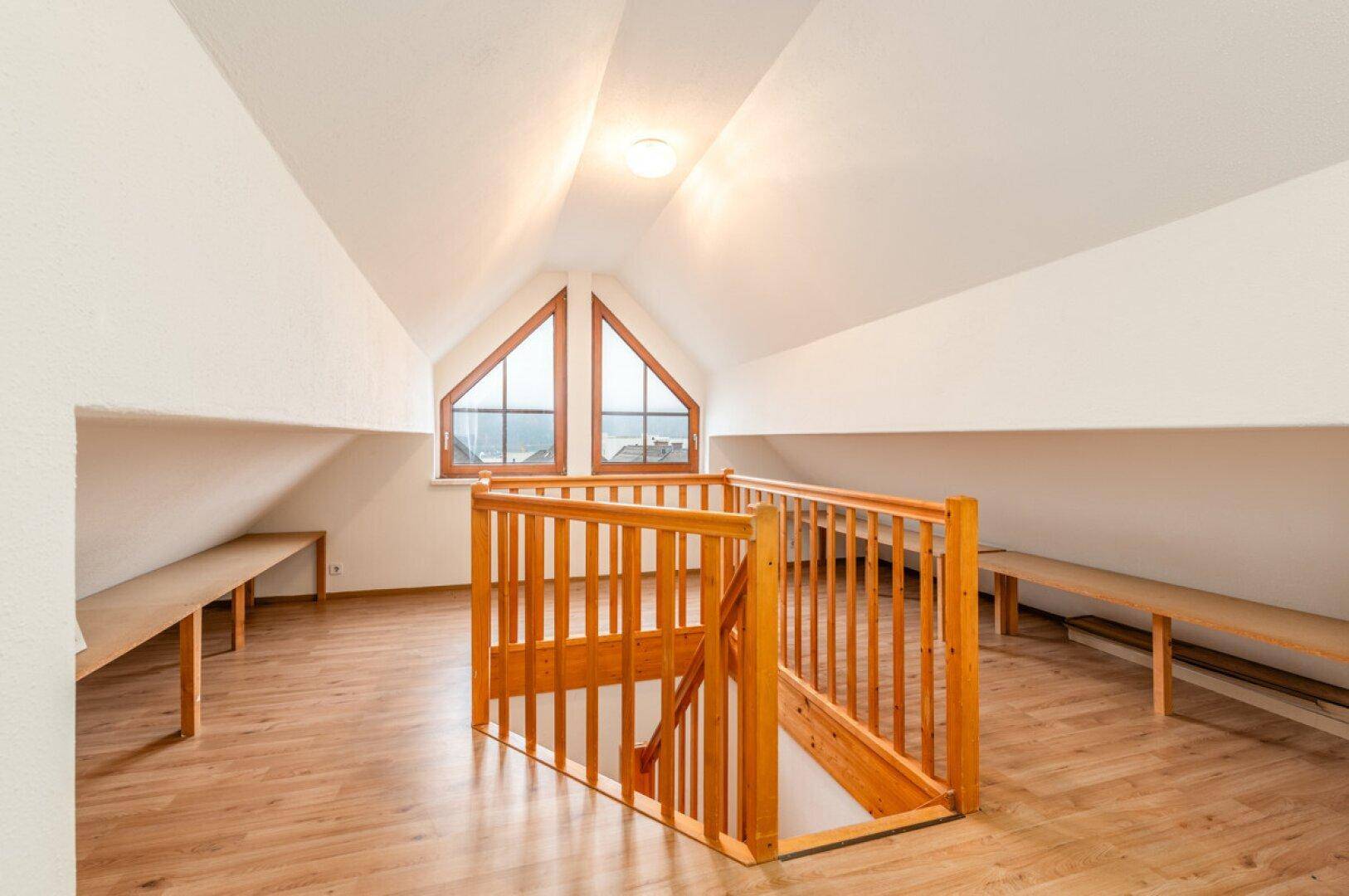 Heller Dachbodenbereich mit Laminatboden, Holzgeländer und einem großen Giebelfenster.