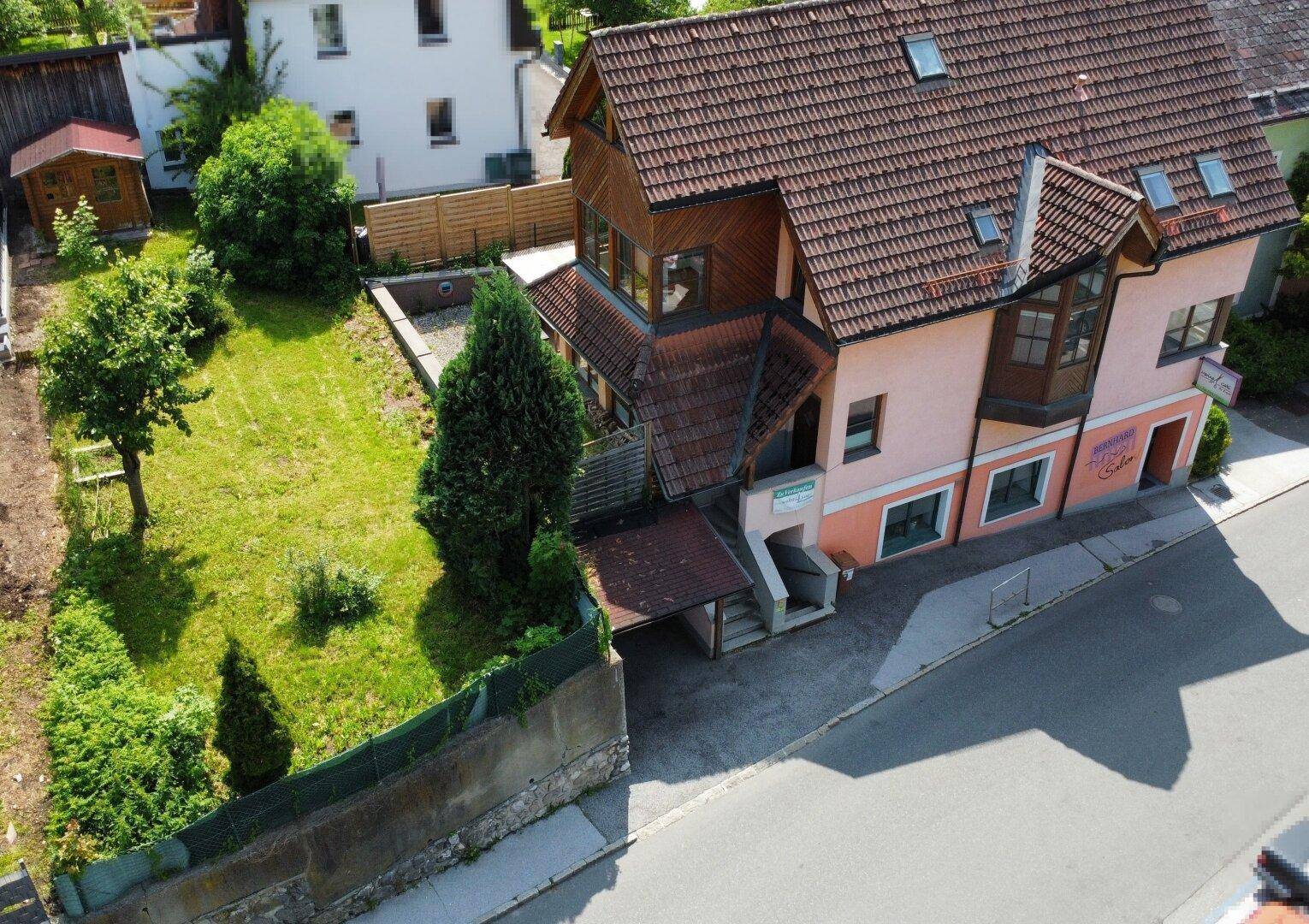 Luftaufnahme des Hauses von der Straßenseite mit Carport und angrenzendem Gartenbereich.