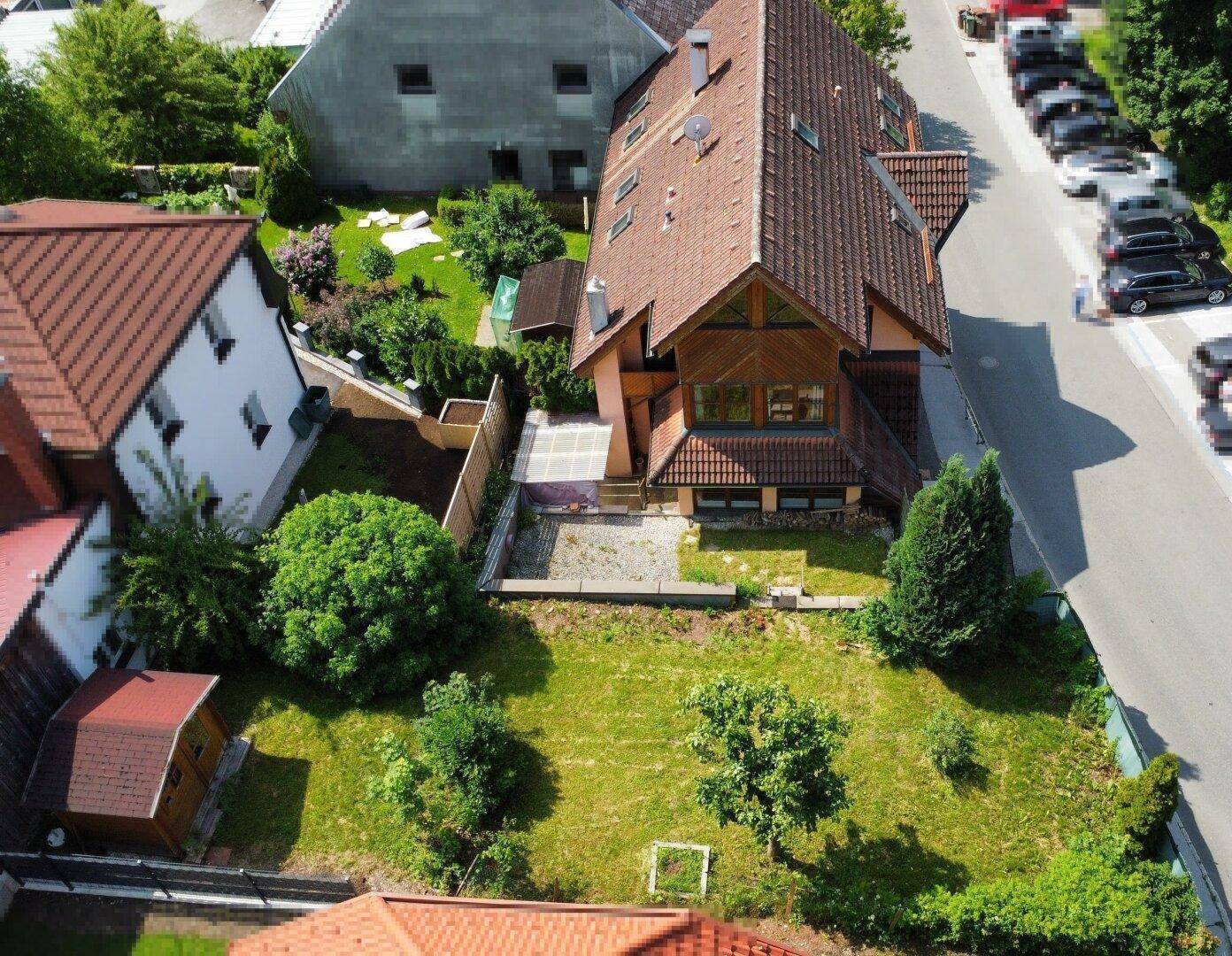 Überblick über das Anwesen mit großem Garten, Terrasse und angrenzender Straße mit parkenden Autos.
