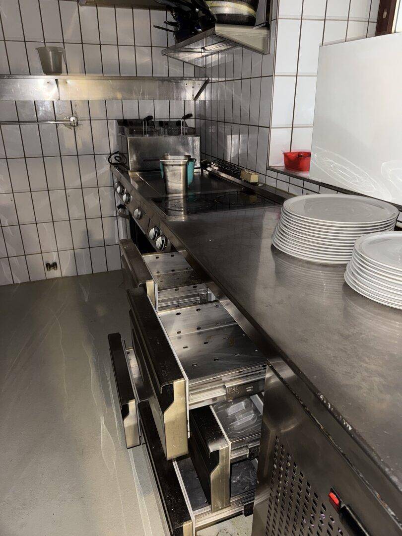 Edelstahl-Arbeitsflächen und professionelle Kochgeräte in einer sauberen, gefliesten Küche.