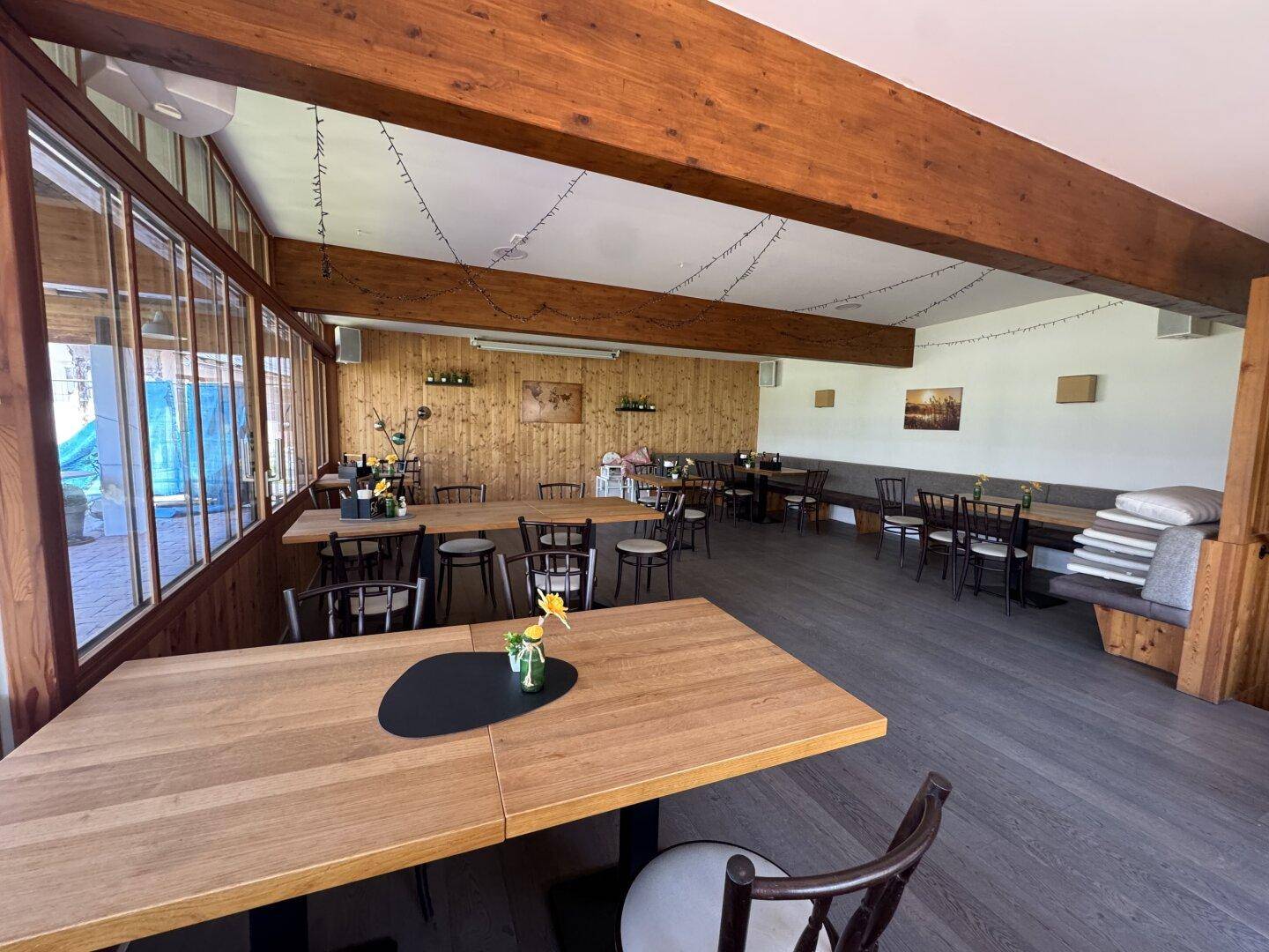 Geräumiger Speisesaal mit Holzbalken, großen Fenstern und vielen Tischen für Gäste.