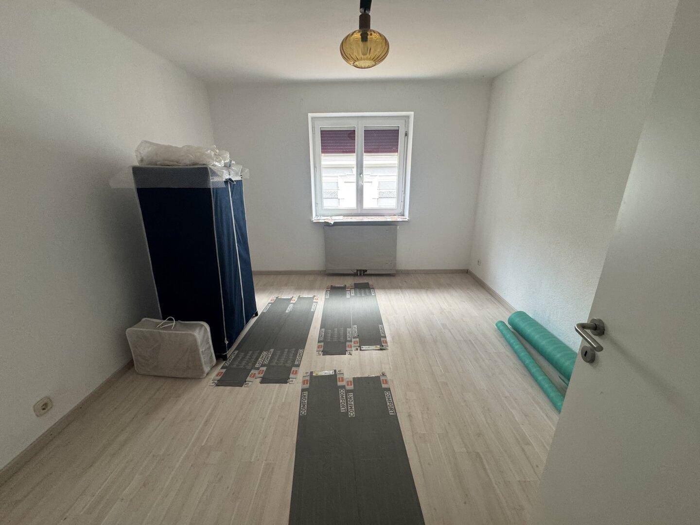 Unmöbliertes Schlafzimmer mit Fenster und neuem Laminatboden, bereit für die individuelle Gestaltung.