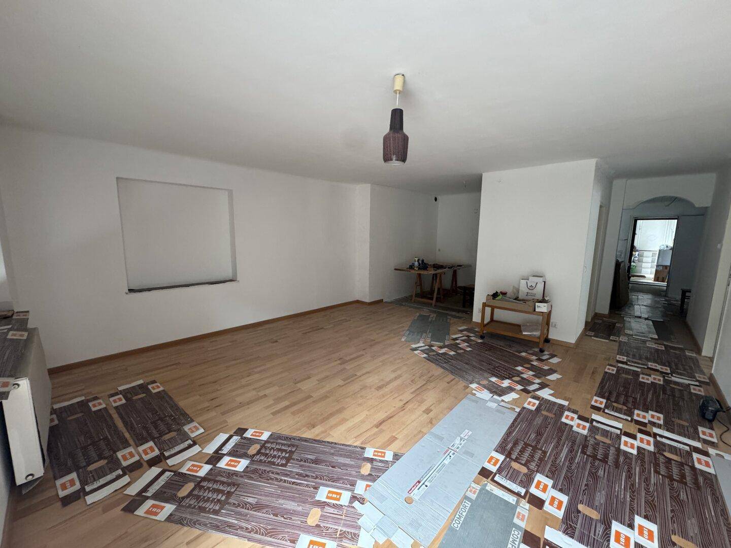 Geräumiges Wohnzimmer mit Holzboden und vorbereiteten Flächen für neue Bodenbeläge.