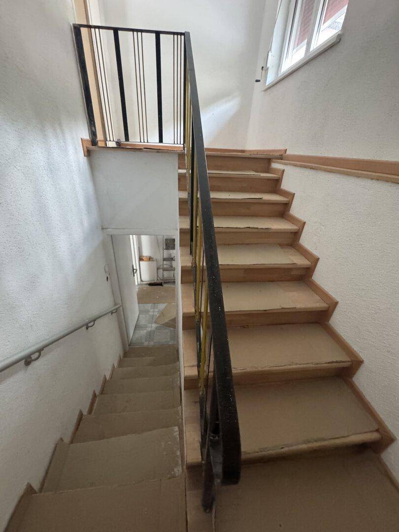 Treppenhaus mit Holzstufen und Geländer, das zu den oberen und unteren Etagen führt.