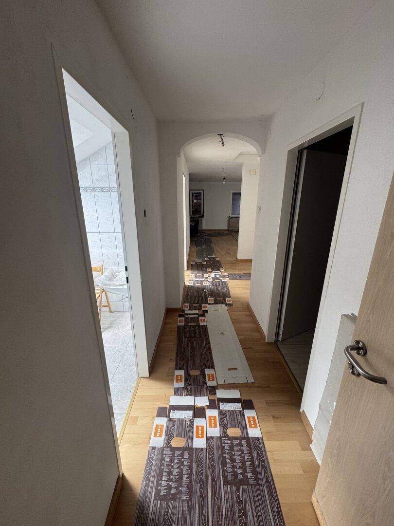 Langer Flur mit Holzboden und Zugang zu verschiedenen Räumen, teilweise mit neuen Bodenbelägen.