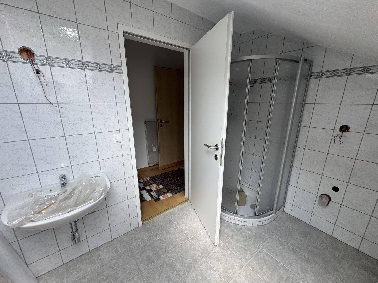 Badezimmer mit Duschkabine, Waschbecken und Fliesen an Wänden und Boden.