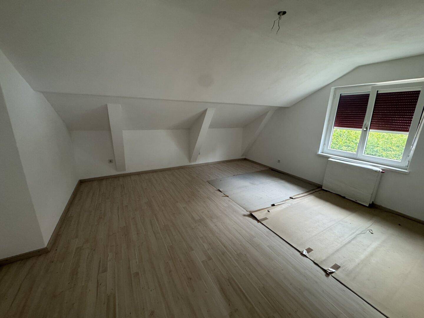 Helles Schlafzimmer im Dachgeschoss mit Fenster und neuem Laminatboden.