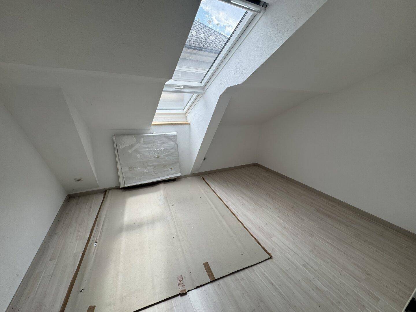 Helles Dachzimmer mit Dachfenstern und neuem Laminatboden, ideal für ein Schlafzimmer oder Büro.