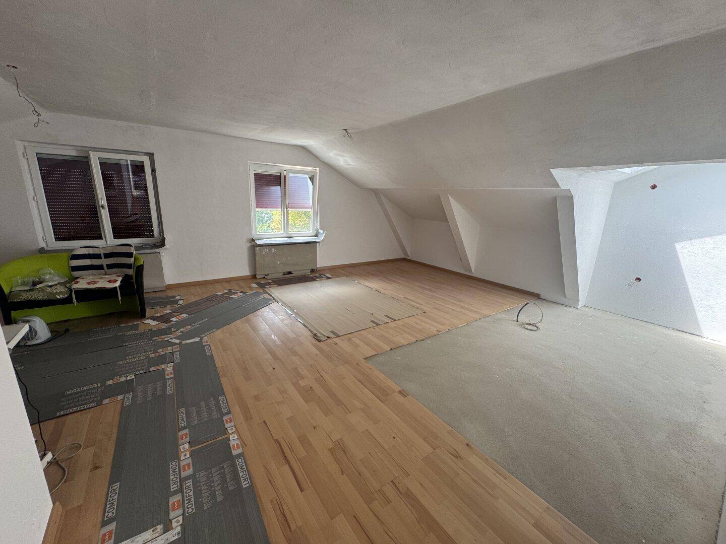 Heller Wohnbereich im Dachgeschoss mit Holzboden und Fenstern, bereit zur Fertigstellung.