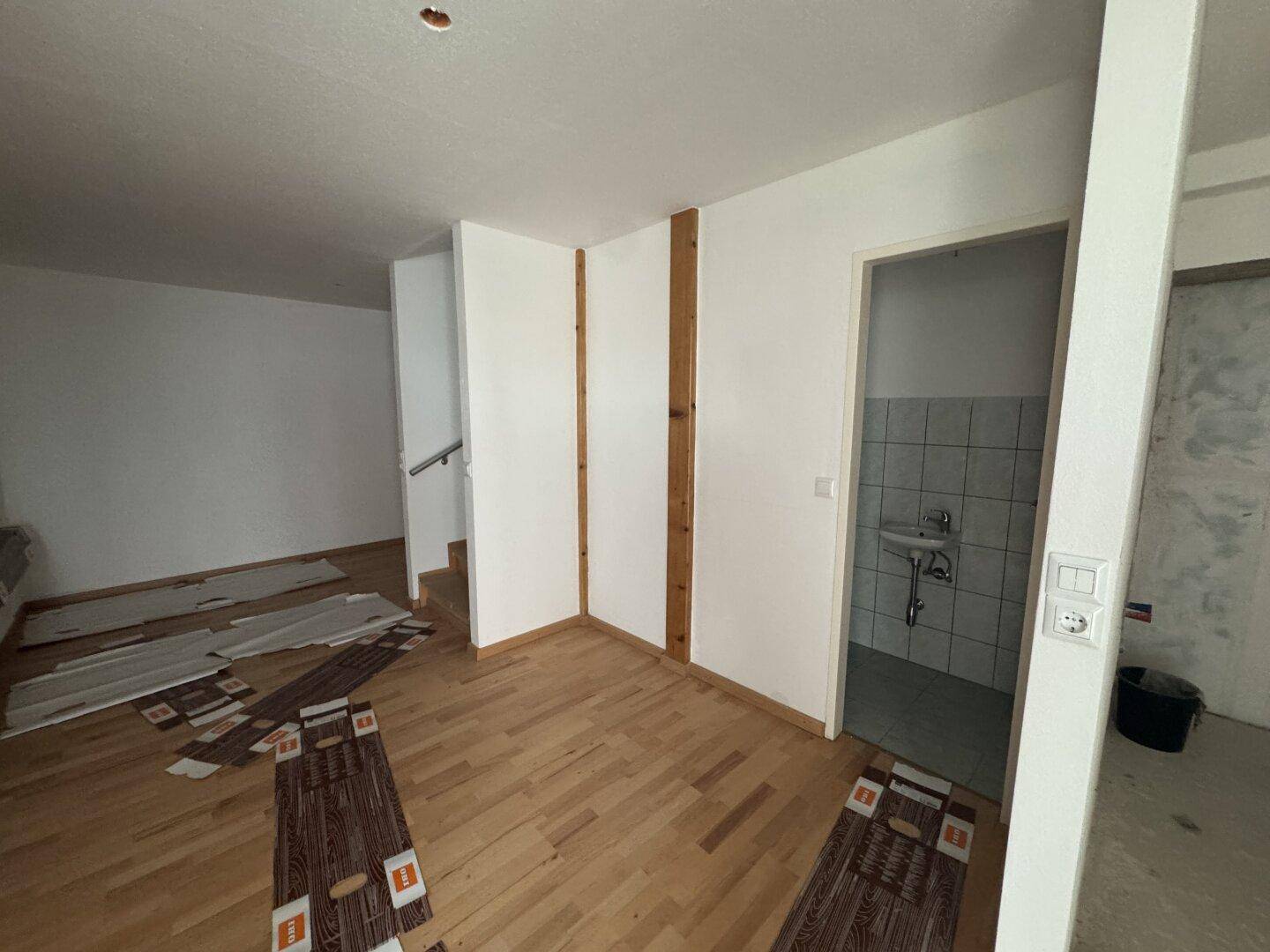 Offener Wohnbereich mit Holzboden und Zugang zu einem kleinen Badezimmer.