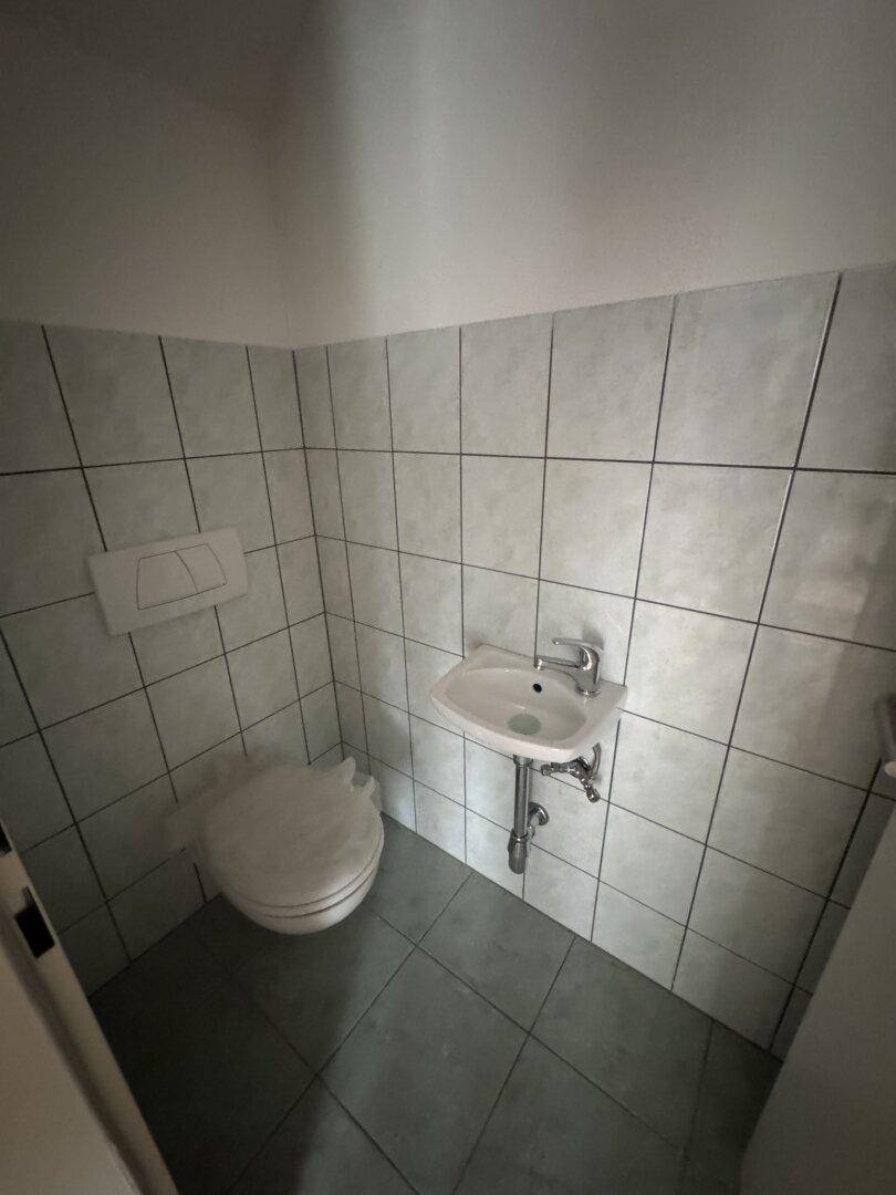 Kleines Gäste-WC mit Toilette, Waschbecken und hellen Fliesen an Wänden und Boden.