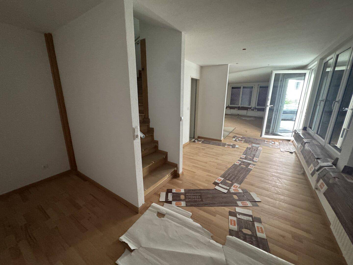 Großer offener Wohnbereich mit Holzboden, Treppe und vielen Fenstern.