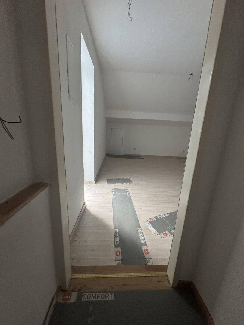 Blick vom Treppenabsatz in einen hellen Raum mit Holzboden und Dachschrägen.