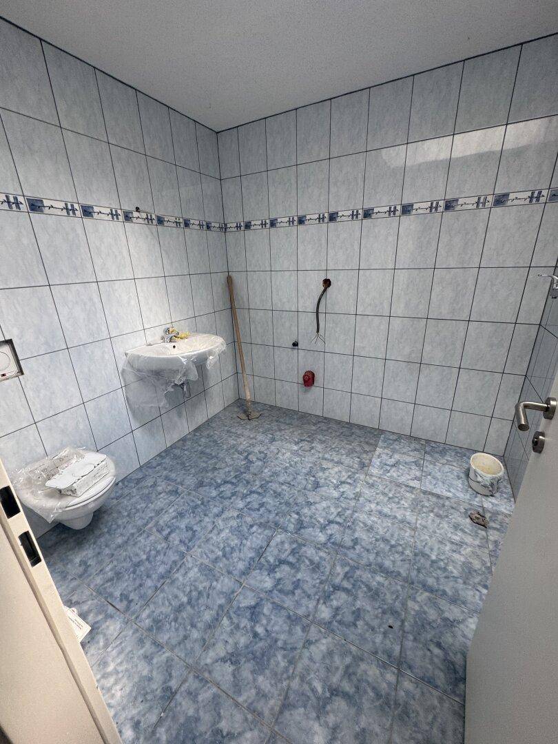 Badezimmer mit blauen Fliesen an Wänden und Boden, Toilette und Waschbecken.