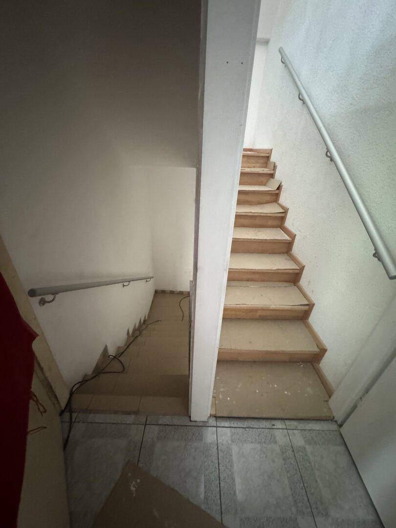 Treppenhaus im Umbau mit Holzstufen und einfachem Handlauf, der Boden ist mit Fliesen ausgelegt.