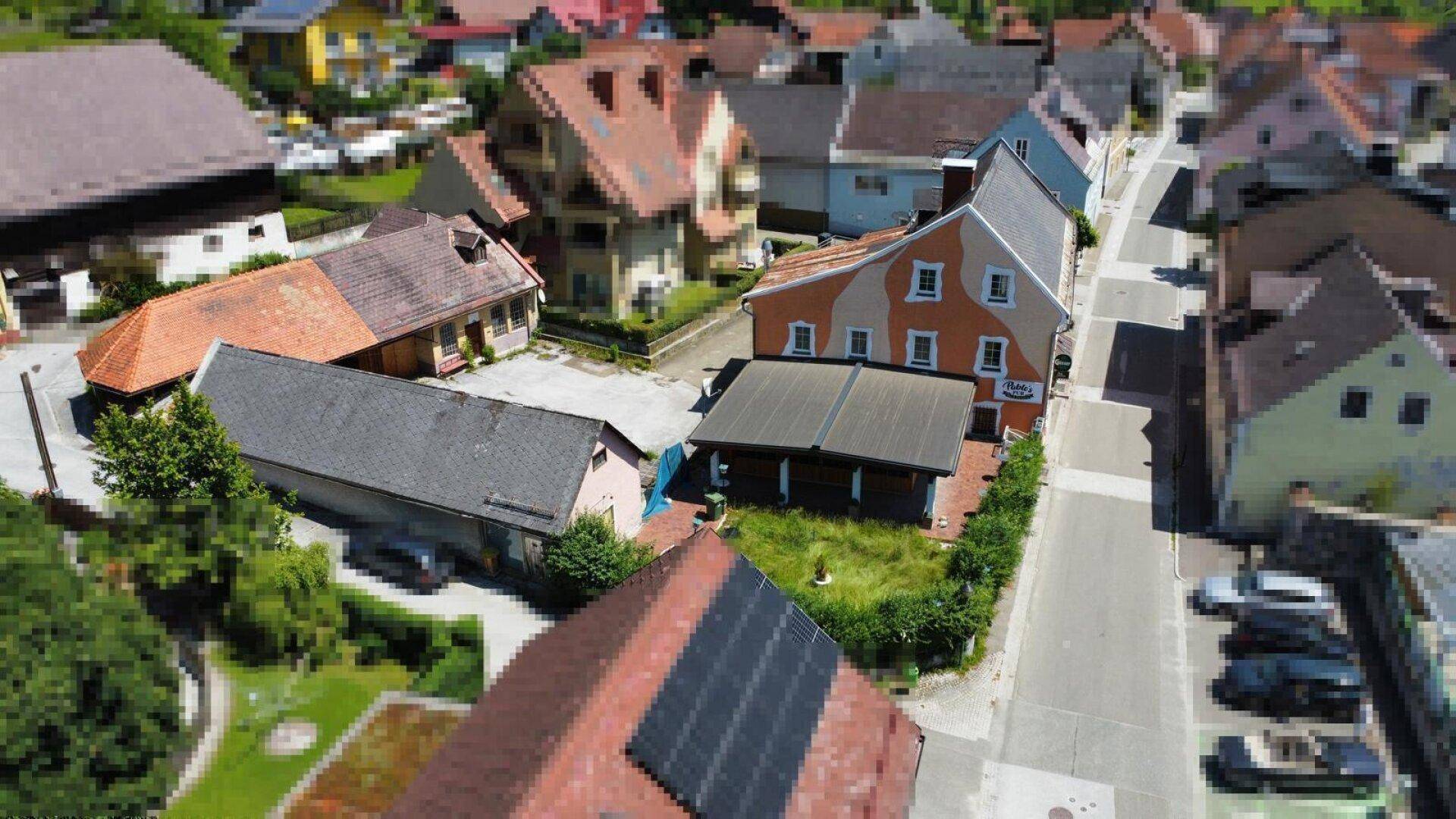 Vogelperspektive des Gebäudes mit orangefarbener Fassade, umgeben von anderen Häusern und viel Grün.