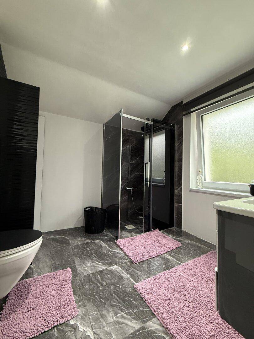Modernes Badezimmer mit Duschkabine, wandhängendem WC und eleganten Marmorfliesen.