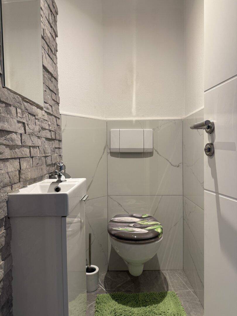 Modernes Gäste-WC mit kleinem Waschbecken, wandhängendem WC und Steinwandakzent.