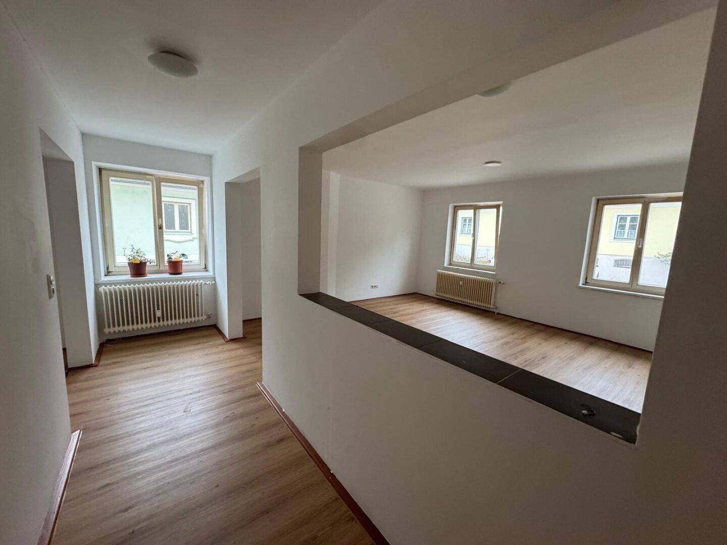 Heller Flur mit Laminatboden und Durchgang zu weiteren leeren Räumen mit Fenstern.