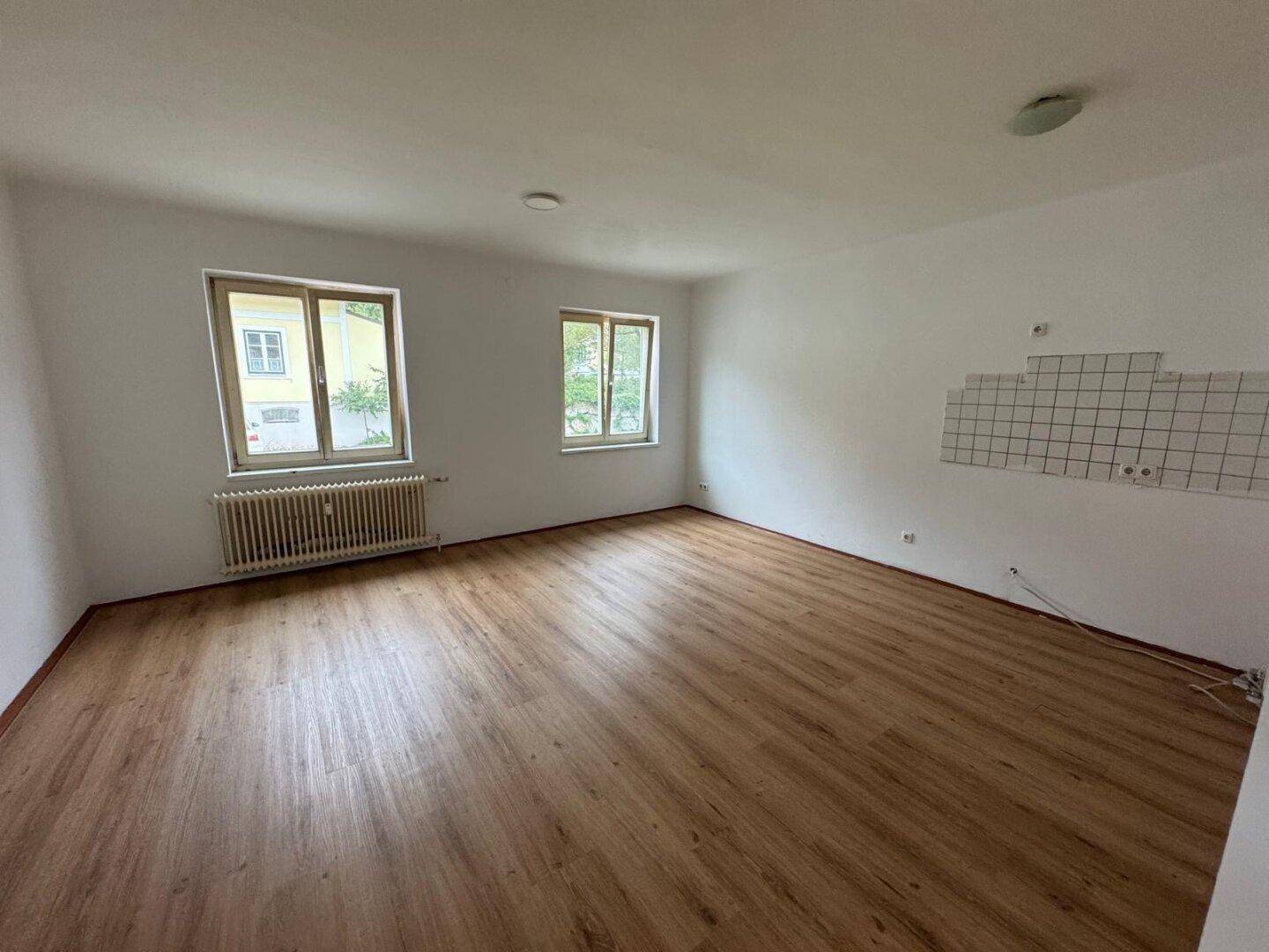 Geräumiges, leeres Zimmer mit Laminatboden und zwei Fenstern, ideal als Wohnbereich.