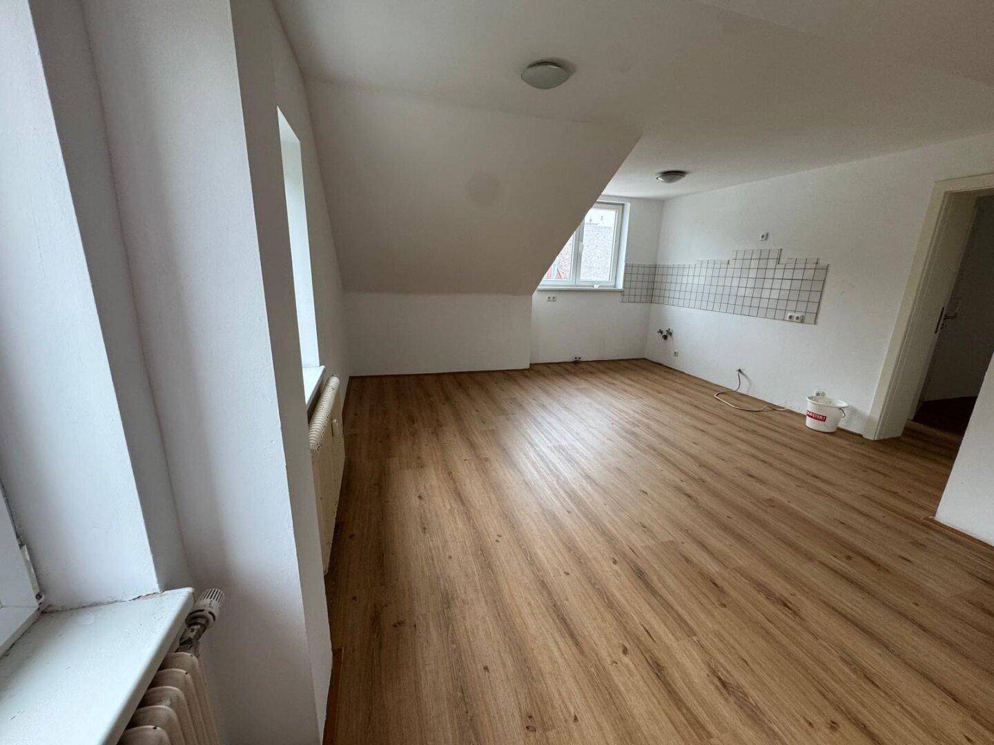 Heller Raum im Dachgeschoss mit Laminatboden, schräger Decke und vorbereiteter Küchenwand.