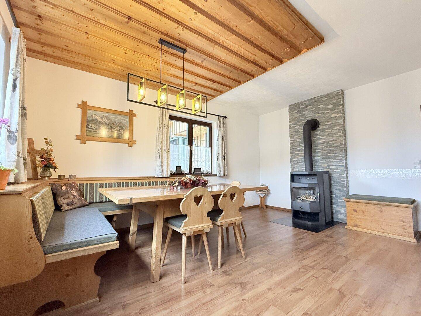Gemütlicher Essbereich mit Holztisch, Eckbank und einem modernen Holzofen für behagliche Wärme.