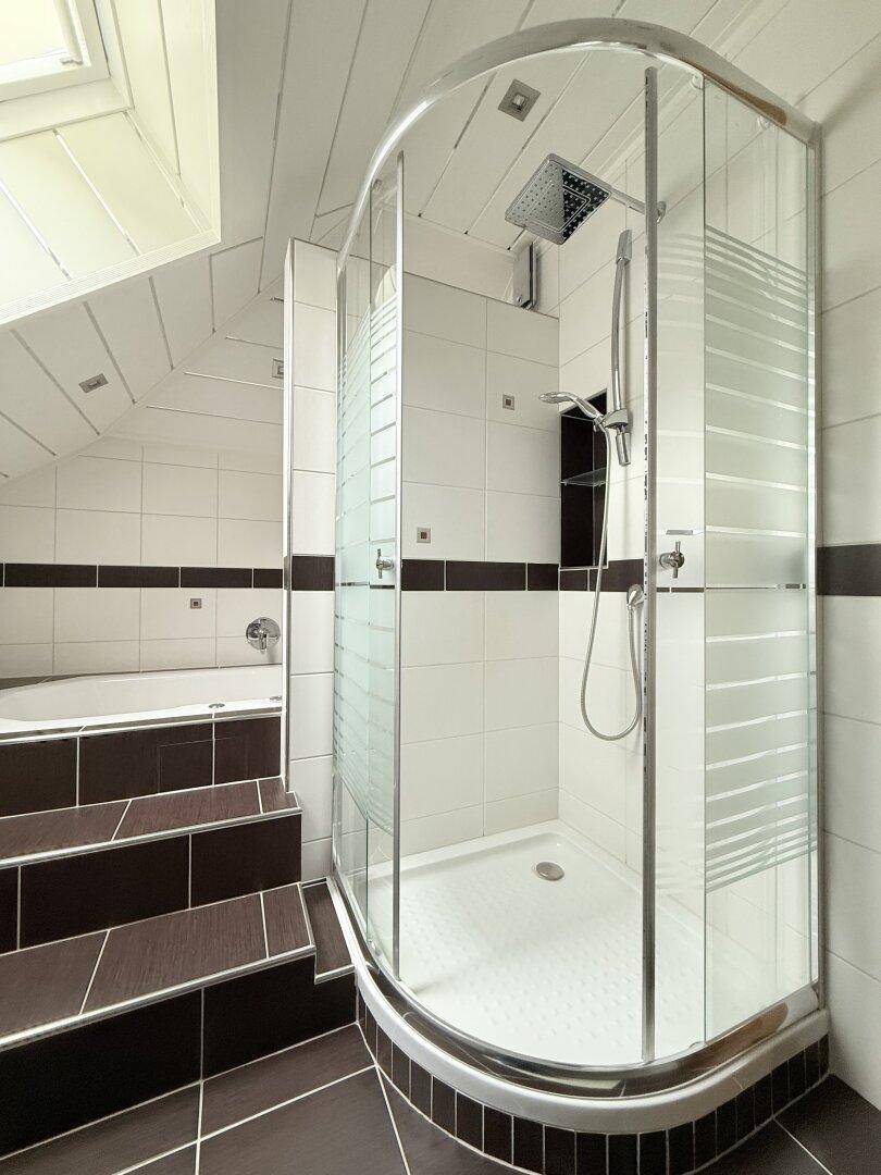 Helle Duschkabine mit Regendusche in einem modern gefliesten Badezimmer mit Dachschräge.