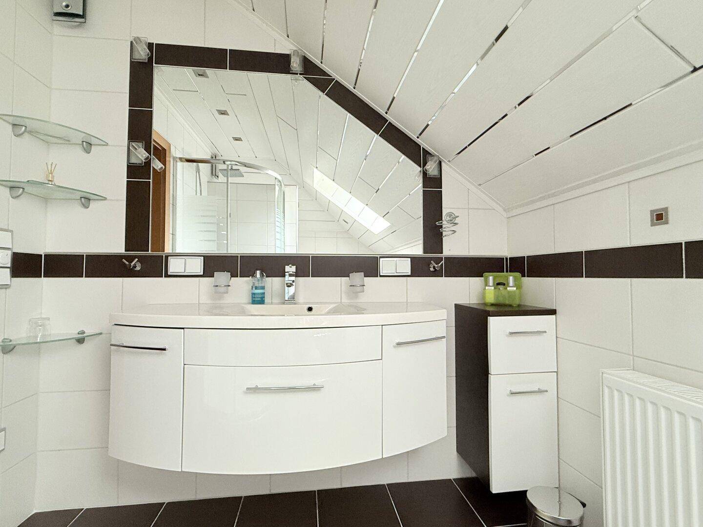 Modernes Badezimmer mit Doppelwaschbecken, großem Spiegel und Dachschräge für viel Licht.