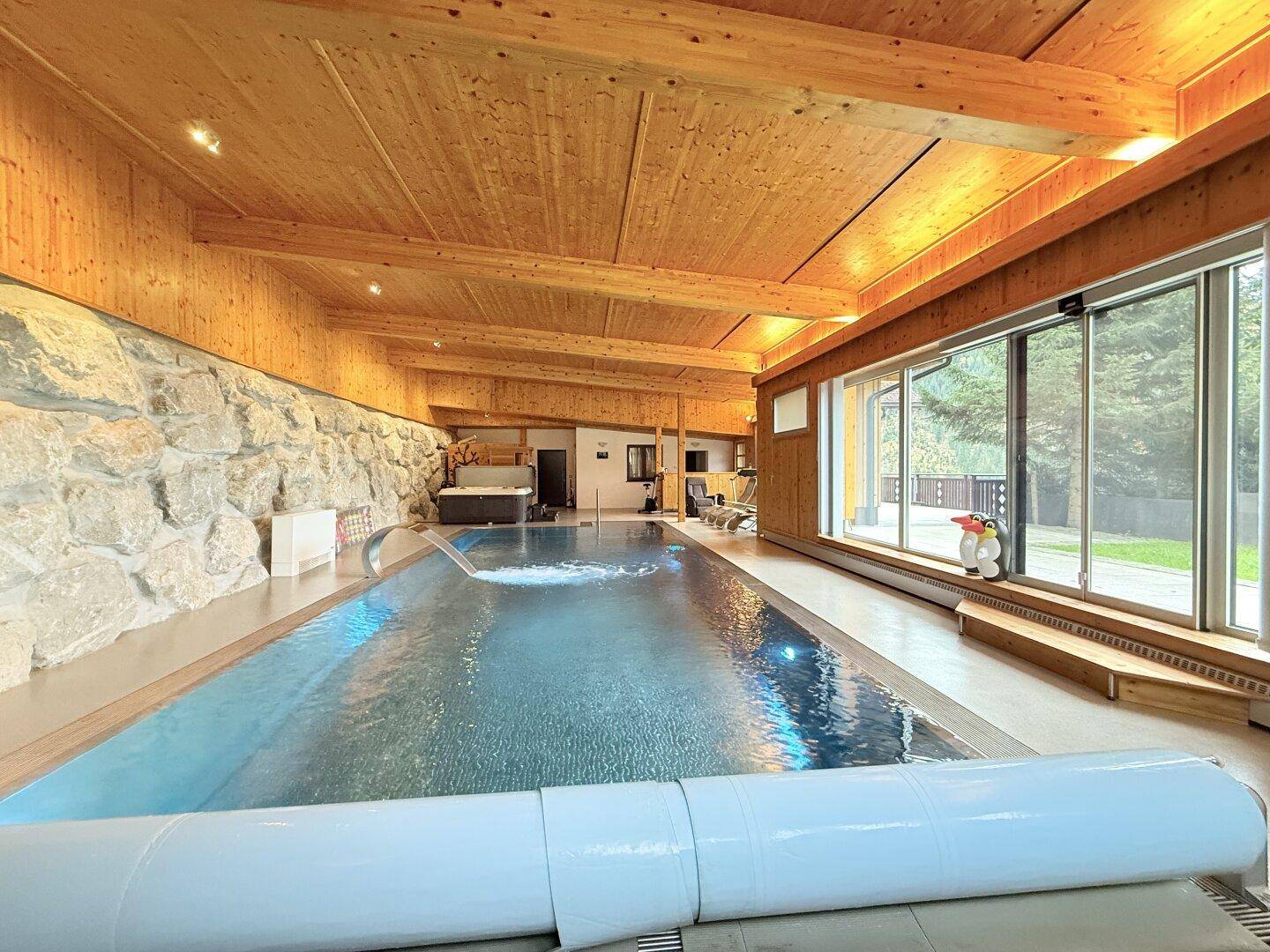 Geräumiger Innenpool mit Steinwand, Holzdecke und Zugang zur Terrasse mit Blick ins Grüne.