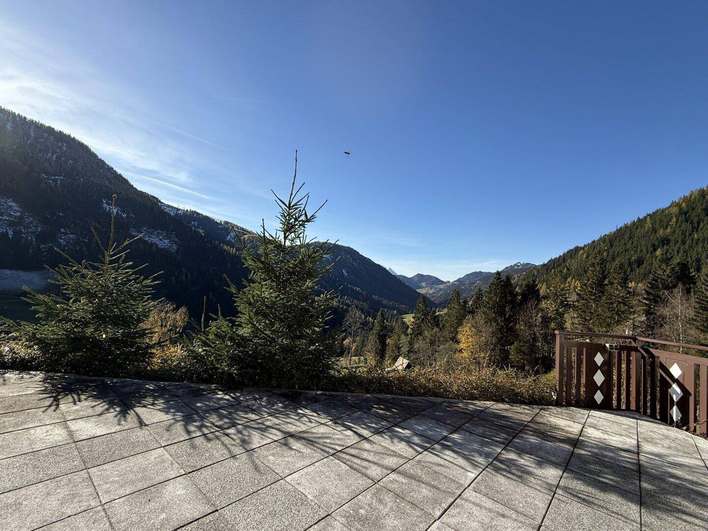 Sonnige Terrasse mit Steinplatten und weitem Blick auf die grüne Berglandschaft.