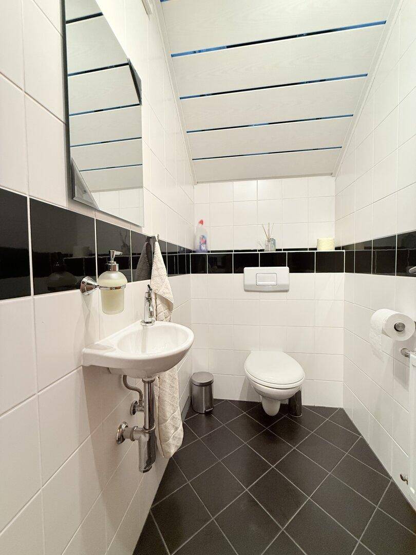 Kleines Gäste-WC mit Wand-WC, Waschbecken und schwarz-weißen Fliesen an den Wänden.