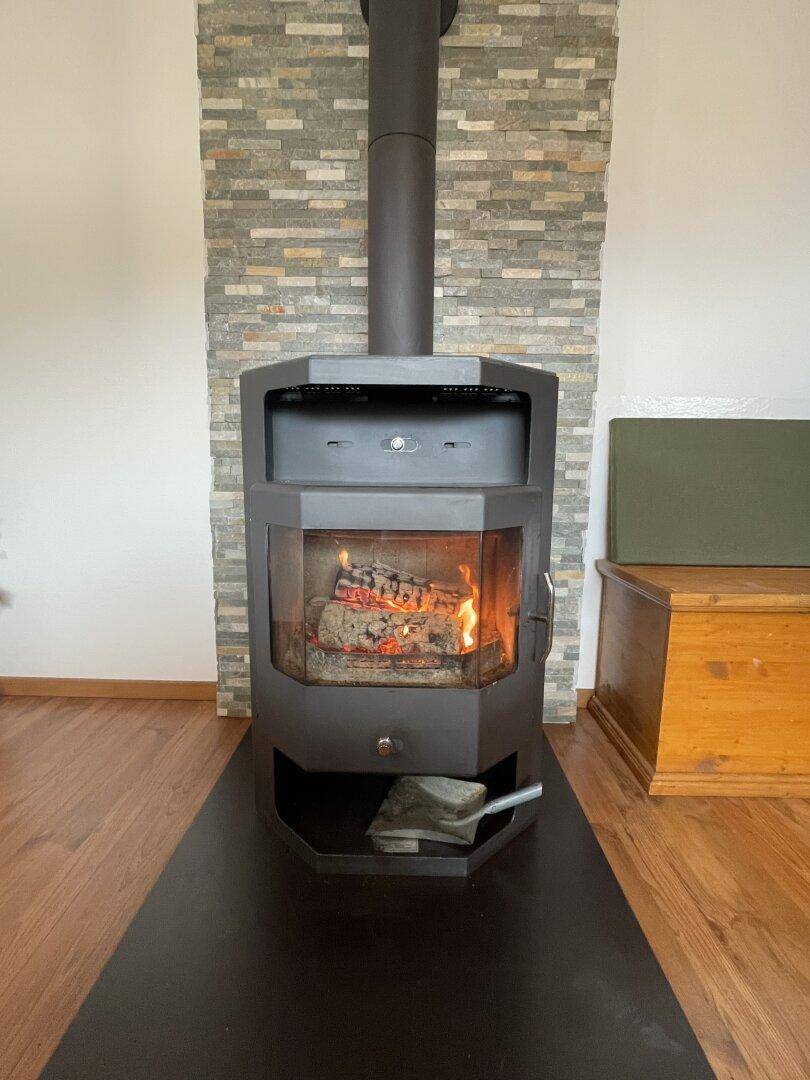 Moderner Holzofen mit sichtbarem Feuer, umgeben von einer Steinwand und Holzboden.