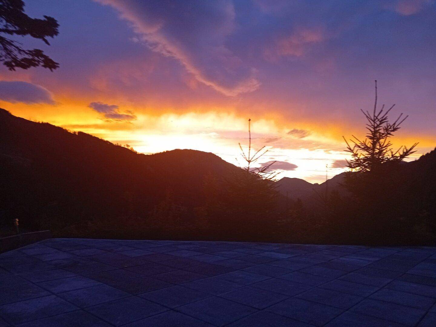 Spektakulärer Sonnenuntergang über den Bergen, gesehen von einer Terrasse mit weitem Blick.