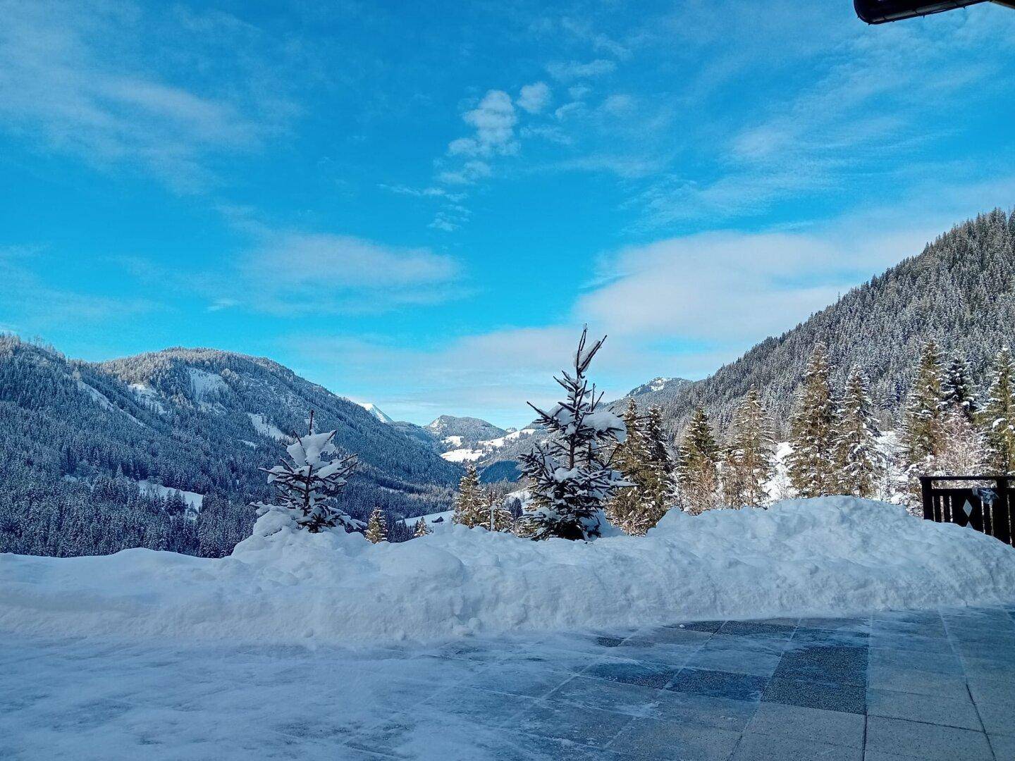 Winterliche Terrasse mit viel Schnee und Panoramablick auf die verschneite Bergwelt.