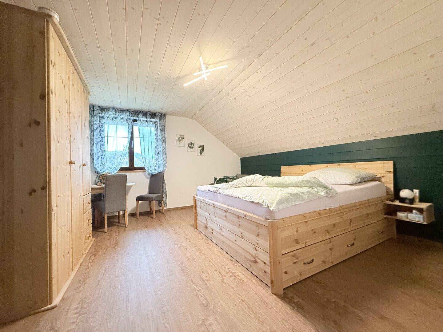 Helles Schlafzimmer mit Holzmöbeln, Dachschräge und Fensterblick in die Natur.