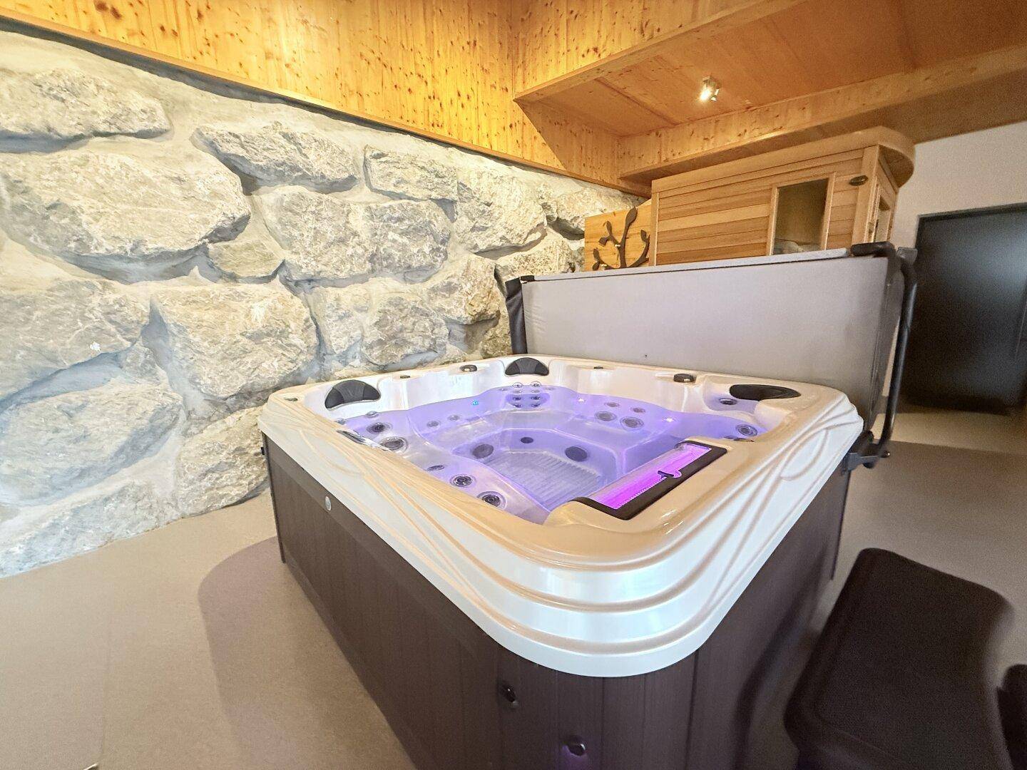 Entspannungsbereich mit Whirlpool, Steinwand und Sauna im Hintergrund für Wellness.