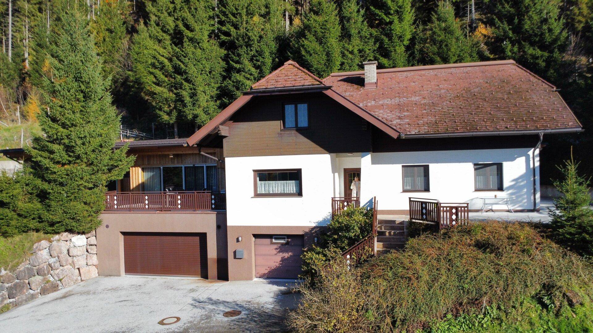 Attraktives Einfamilienhaus mit Satteldach, Garage und Balkon in grüner Bergumgebung.