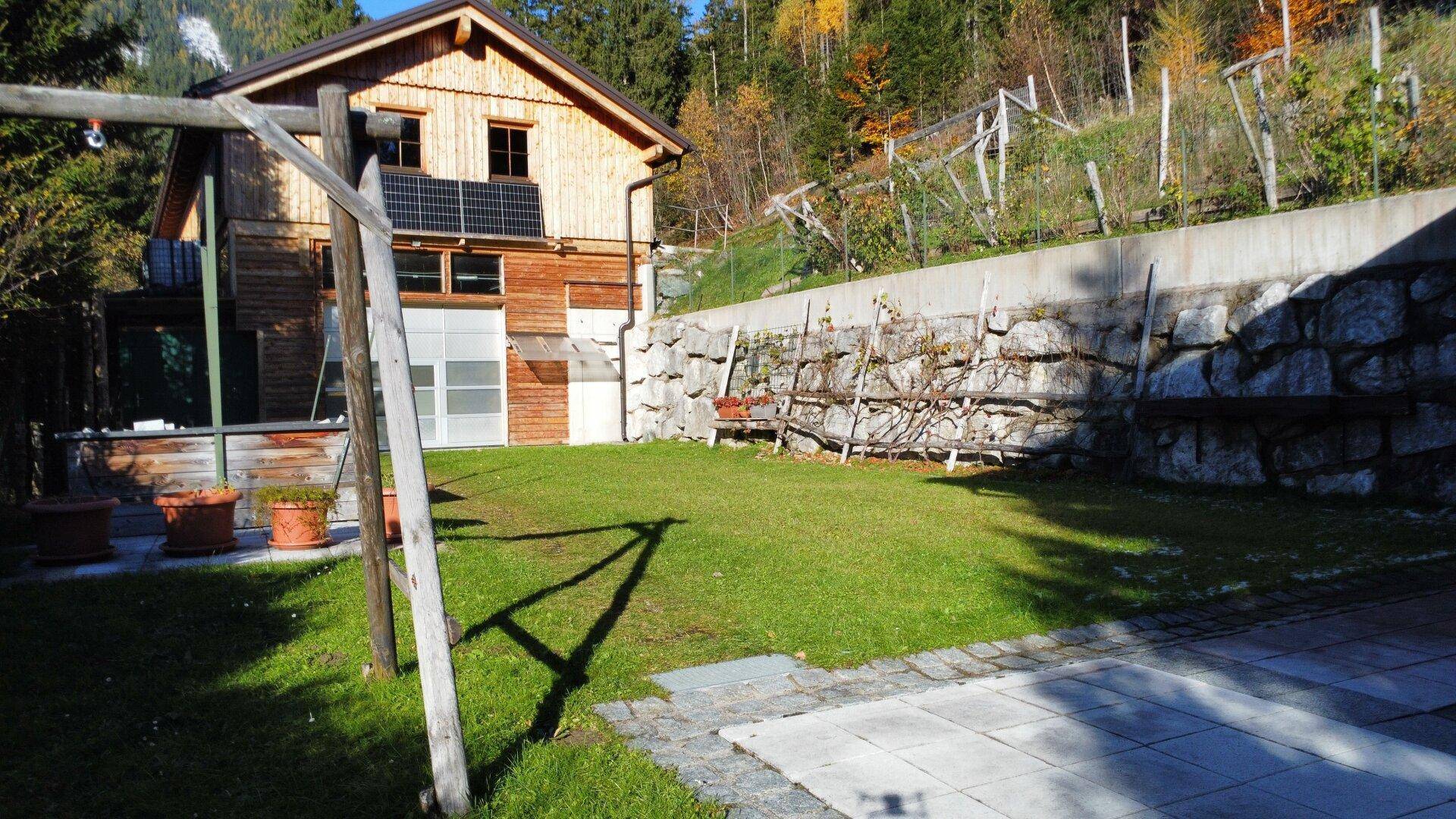 Gepflegter Gartenbereich mit Rasenfläche, Steinmauer und traditionellem Holzhaus im Hintergrund.