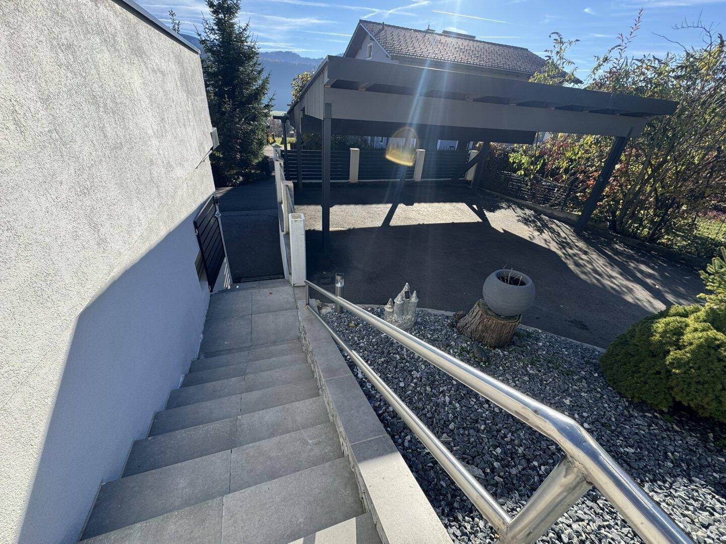 Außentreppe mit Edelstahlgeländer führt zur Zufahrt und dem überdachten Carportbereich.