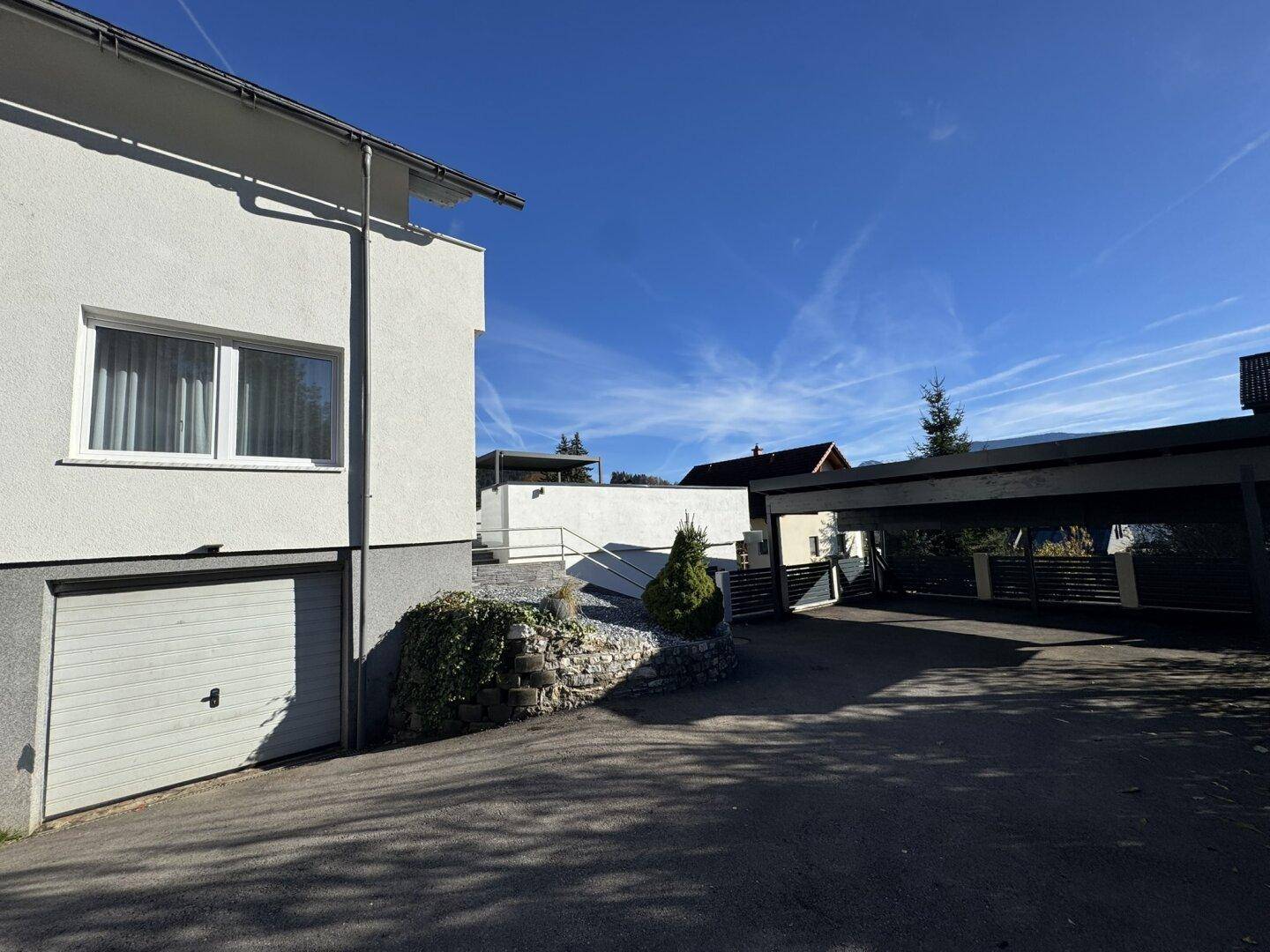 Seitenansicht des Hauses mit integrierter Garage und Zufahrt zum überdachten Stellplatz.