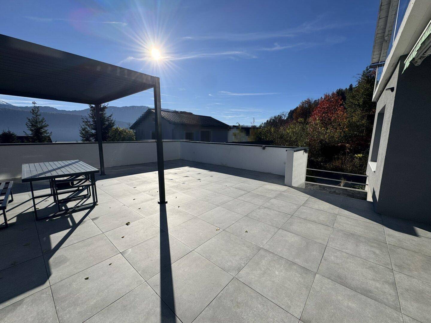 Helle, sonnige Terrasse mit moderner Pergola und weitem Blick in die umliegende Landschaft.