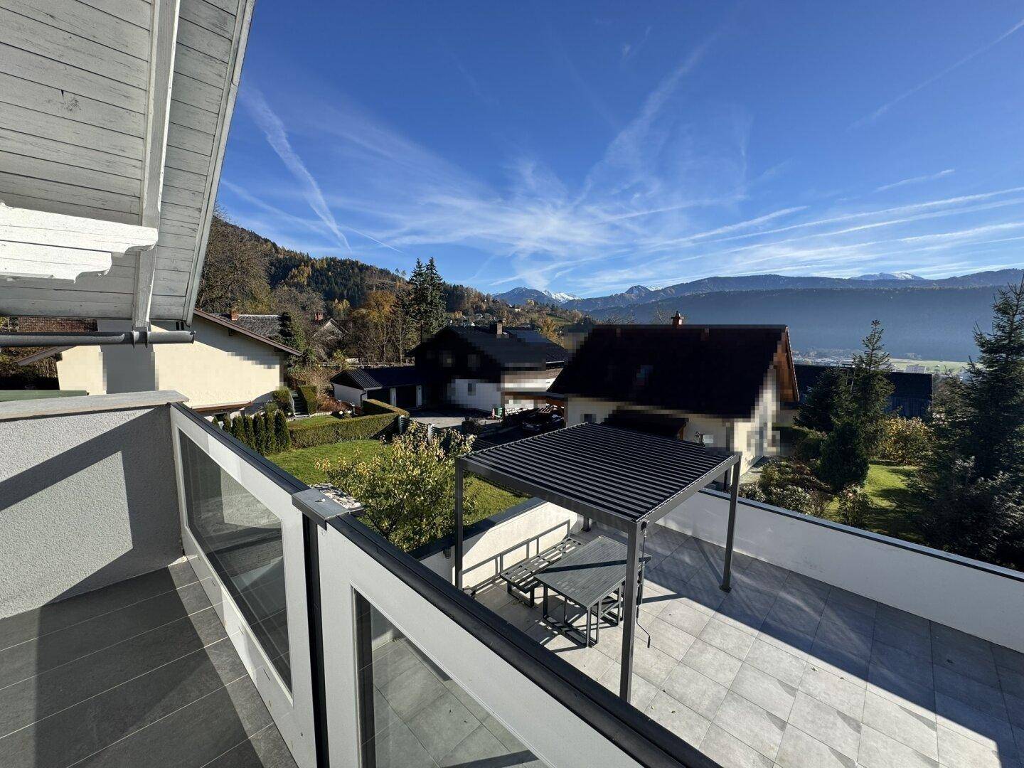 Aussicht vom Balkon auf die Terrasse mit Pergola und die malerische Berglandschaft im Hintergrund.